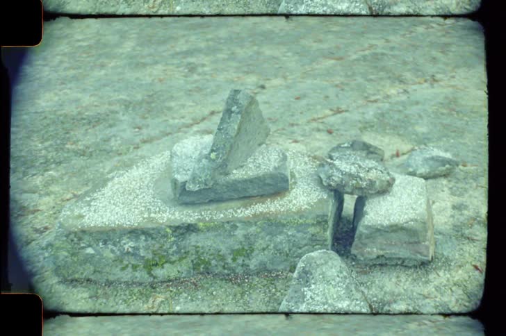 A weathered stone structure lies on a rocky surface under soft lighting