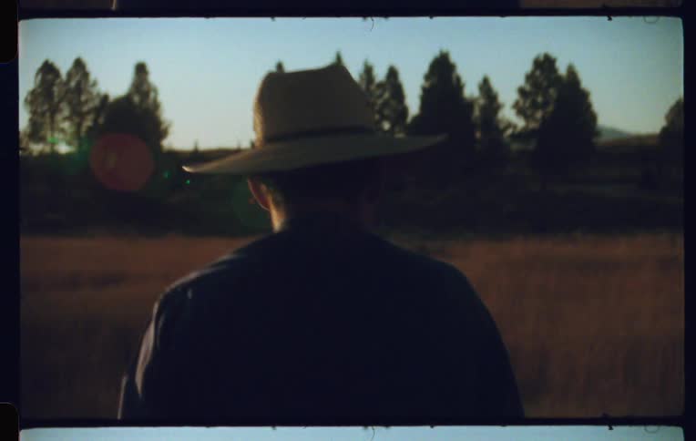 Back view of a man with a hat walking in a field