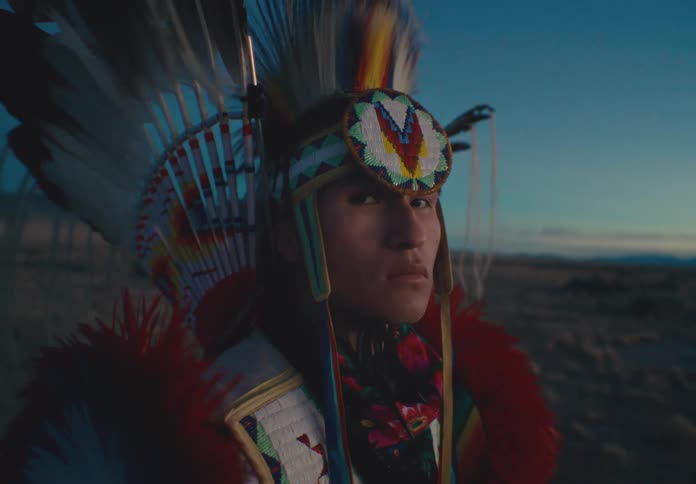 Portrait of a man wearing traditional native american clothing while standing in a field setting one morning