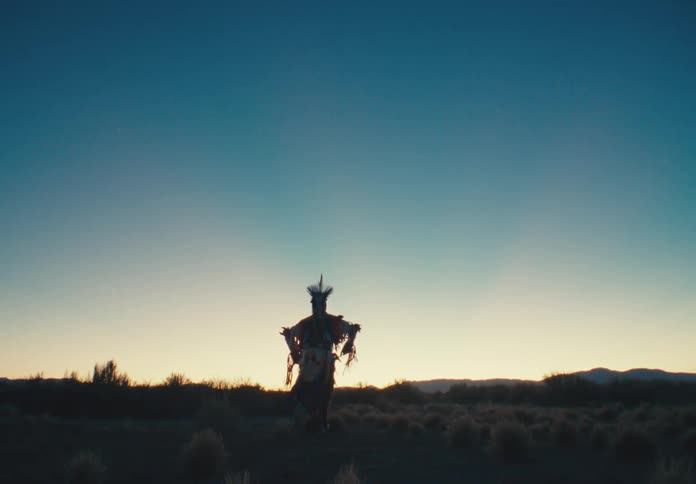 A silhouetted native american dancer in elaborate regalia performs a dance at sunrise in a vast open desert