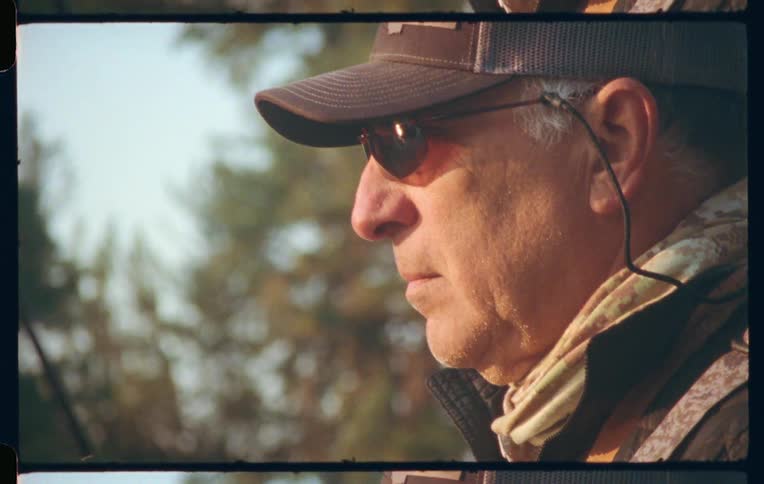 Side portrait of a man with glasses in an outdoor setting with a fishing rod