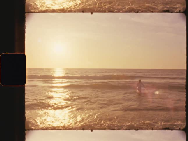 A surfer is entering the sea water with some small waves breaking and he is jumping over them i just is strong in the sky