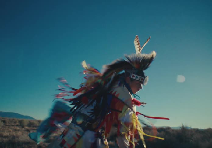 A dancer in colorful ceremonial costume against a bright sunlit backdrop