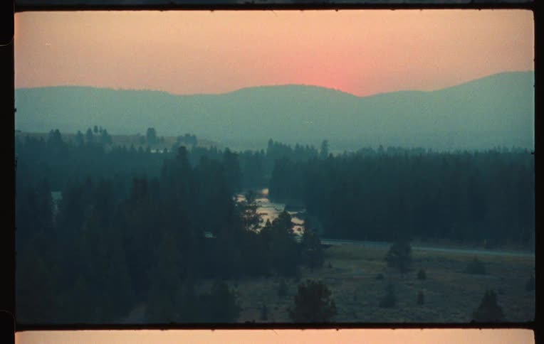 Landscape of a river flowing in an environment surrounded by conifers with mountains in the background