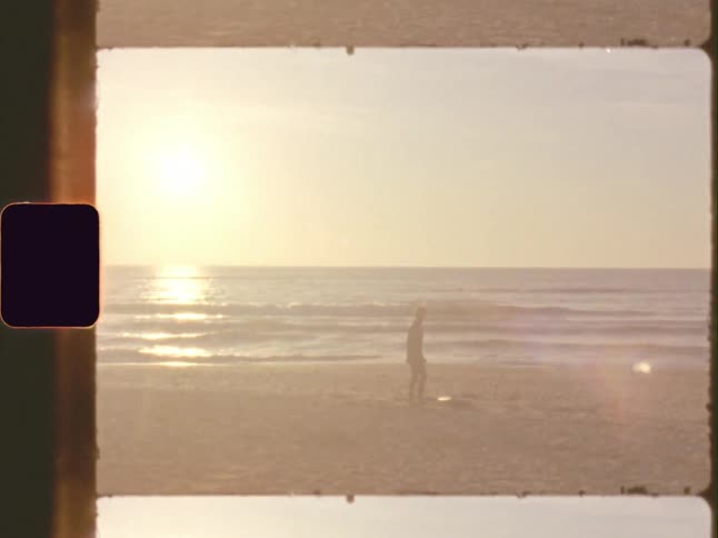 A man stands on a beach at sunset