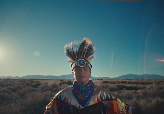 Boy in a colorful traditional dress with feathers in a field with mountains in the background