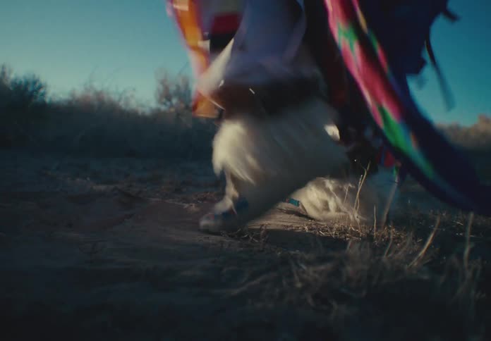 Dancer wearing traditional native american attire dances outside on dusty ground during the day