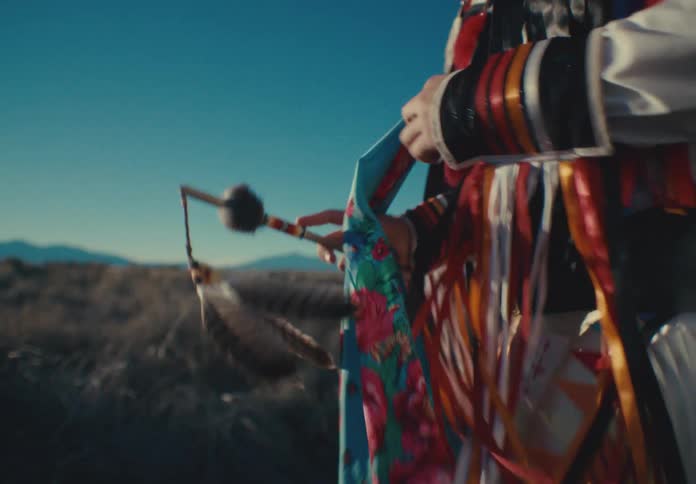 A person holding an object made of feathers on the ends and she is wearing an outfit with colorful ribbons and is shaking herself
