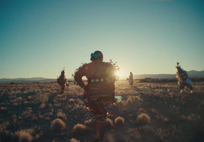 Small group of tribespeople dancing in a desert field with the sun on the horizon