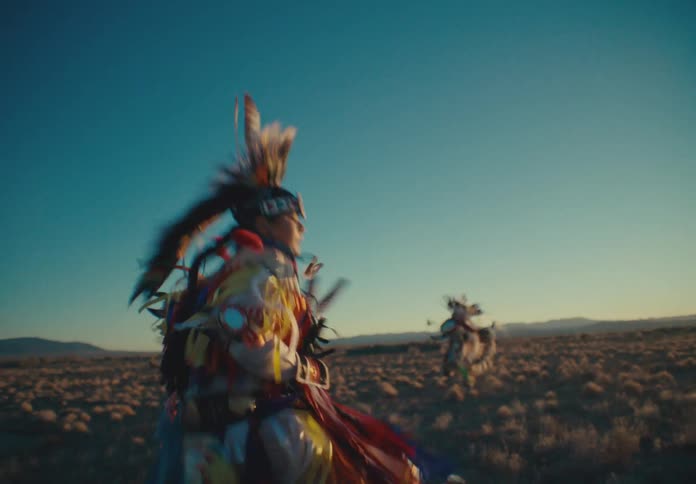 Three native americans are dancing in a grassland at sunset