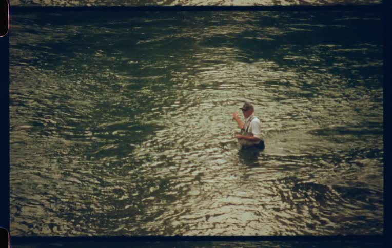 A man in a cap is in a lake and is fishing