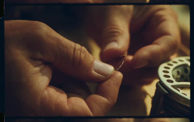 Close up shot of hands meticulously tying fishing line to a hook near a fly fishing reel