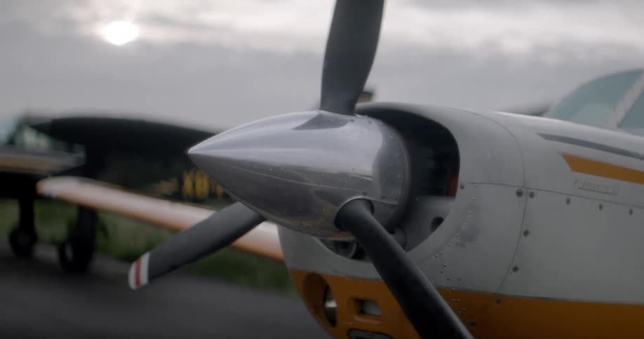 A small planes propeller sits still against a cloudy sky at the airport