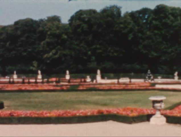 A formal garden with statues flower beds and a gravel path