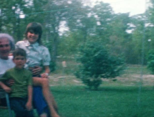 A grandmother is sitting on a chair in the backyard with her granddaughter and grandson