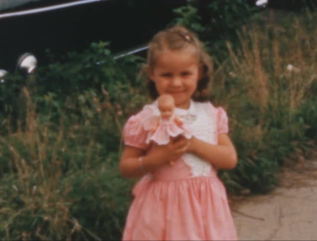 Little girl in a pink dress in an outdoor area holding a doll