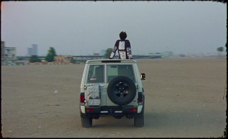 A man is sitting on top of the vehicle as it drives around in the sand