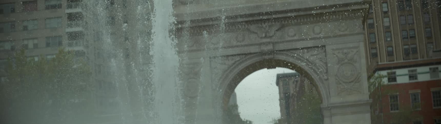 A water fountain near a monumental arch sends up sprays of water