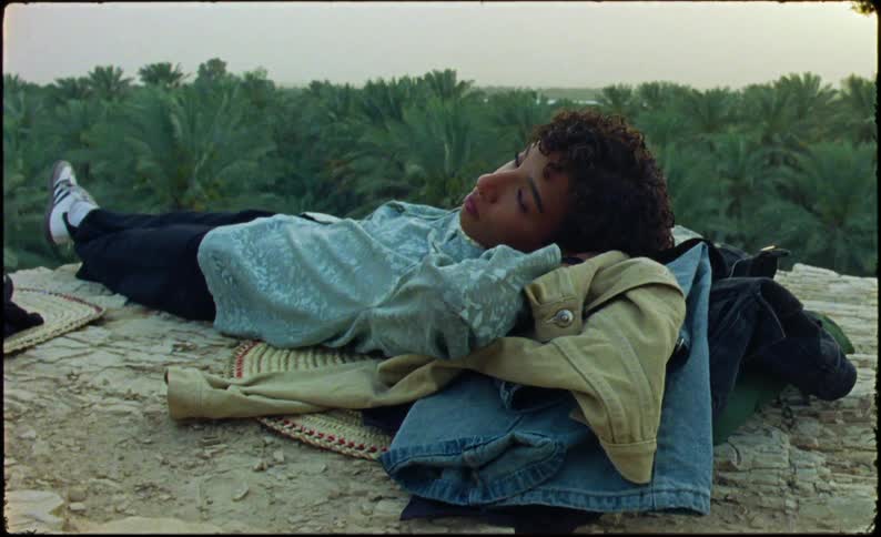 A woman is laying by the edge of the cliff near a forest