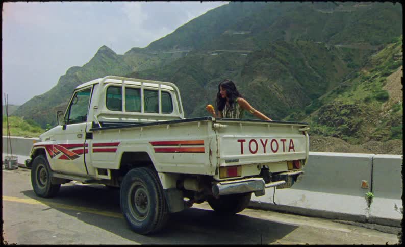 A woman holds up a piece of fruit by the truck