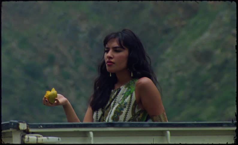 Woman eating a fruit in an outdoor area with green mountains in the background