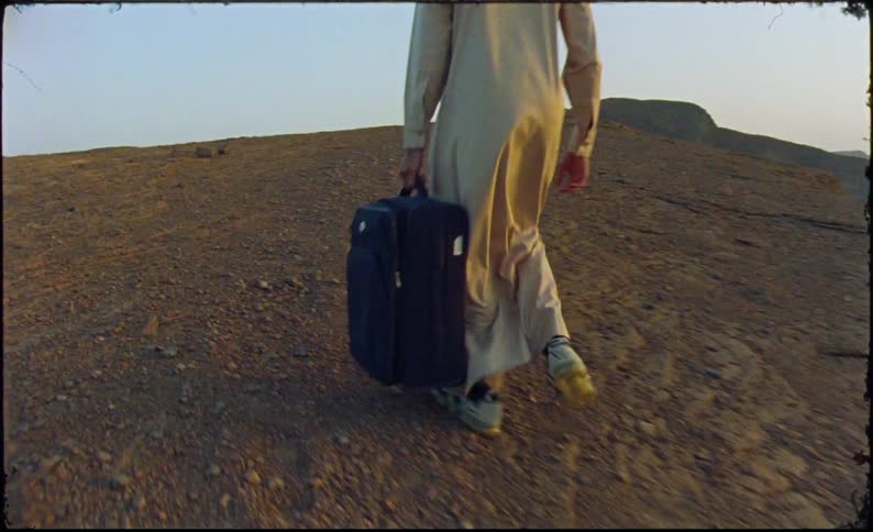 A man is carrying luggage in the desert