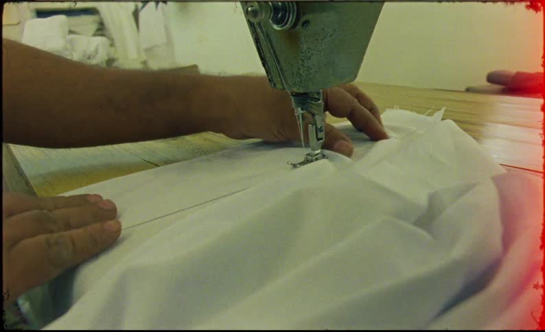 A man operates a sewing machine skillfully stitching a shirt with focused concentration and precision
