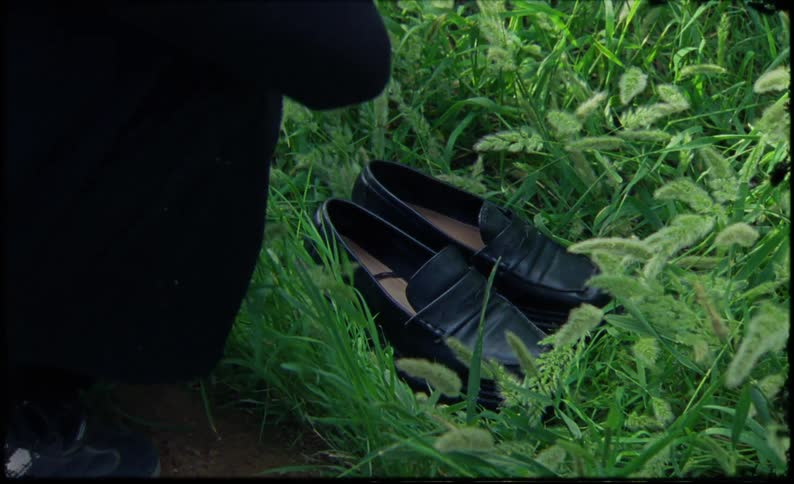 A person picks up black shoes from the grass