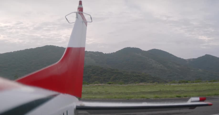 The tail section of a small aircraft with a red and white color scheme positioned on a rural runway
