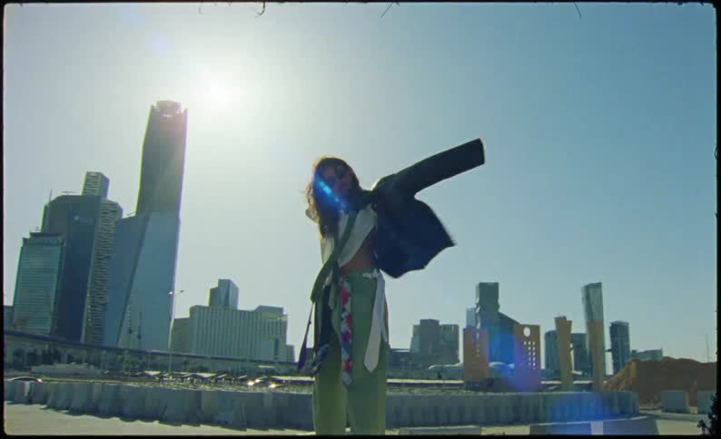 A woman holding a jacket and putting it on in front of a city scape