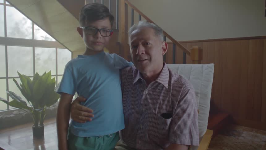 A father sits on a chair in the living room with his son standing beside him
