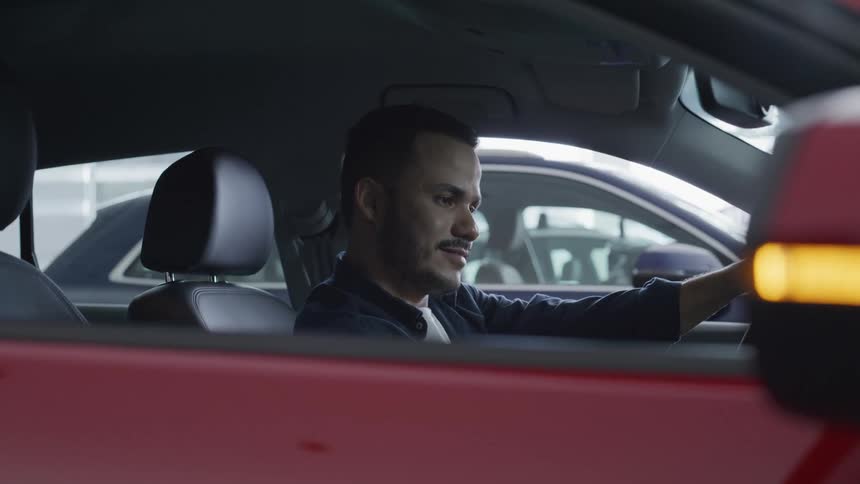 A man is seated inside a red car holding the steering wheel