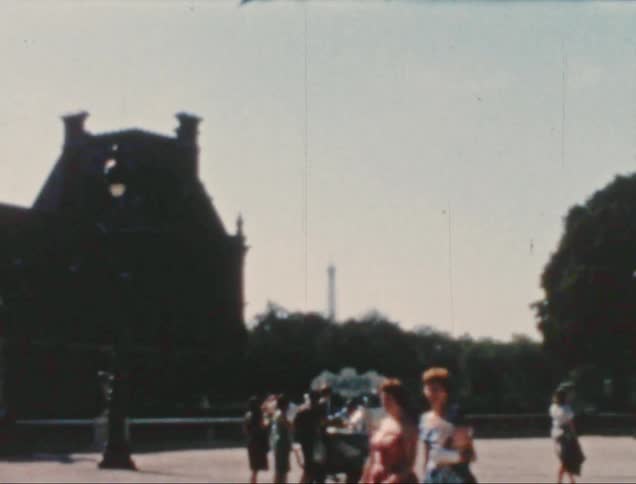 A group of people are walking near a historic building with distinctive architecture possibly a clock tower and a vendor cart in a public square