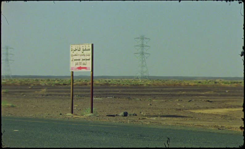 Sign next to a highway in a desert environment with power towers in the background