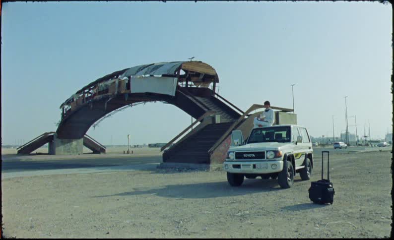 Man sitting on the roof of a car next to a highway with vehicle traffic