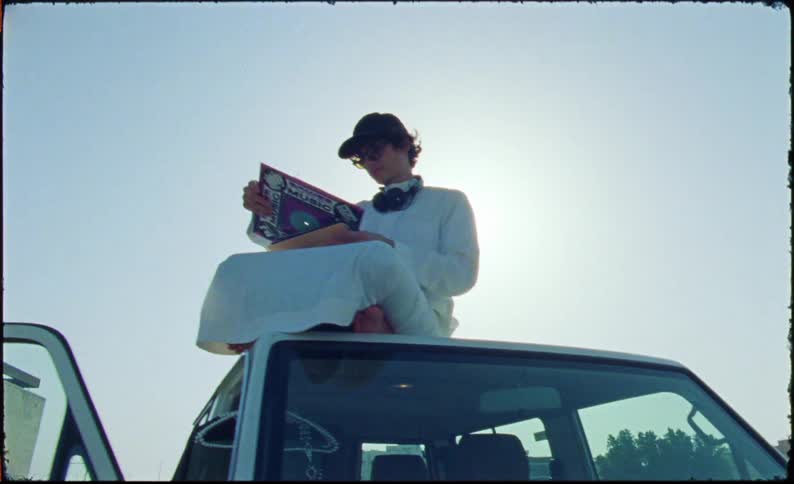 Man sitting on the roof of an open car flips through record albums