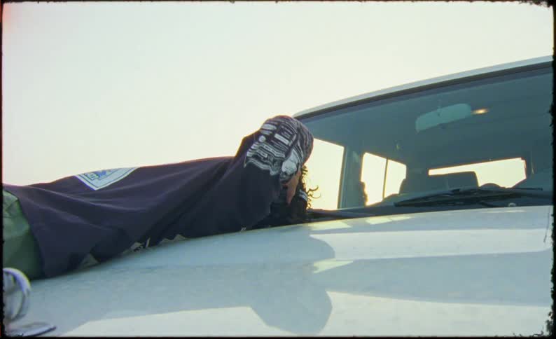A teenager lays on the hood of a white vehicle listening to music