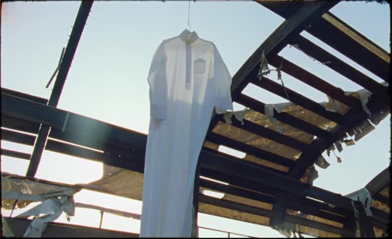 A arge white garment hanging from a roof that is destroyed and it is moving because of the wind