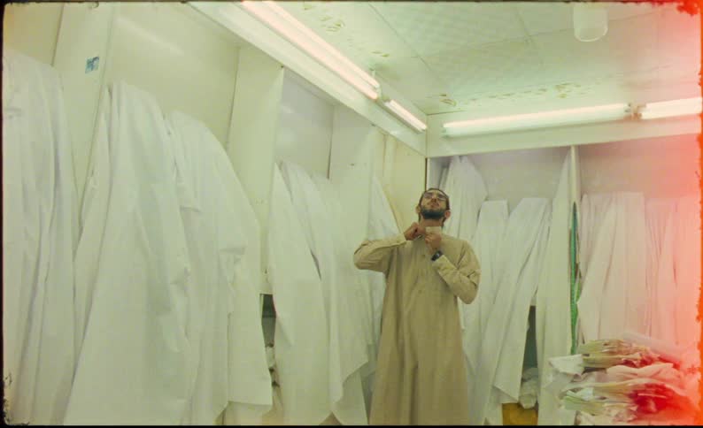 Man standing in a workshop containing draped fabric adjusts his collar