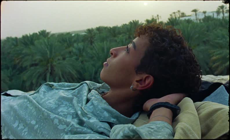 Androgynous person laying on a straw roof with the jungle behind them