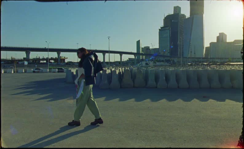 A woman walking to one side holding a black jacket and then she puts it on and starts walking to the other side