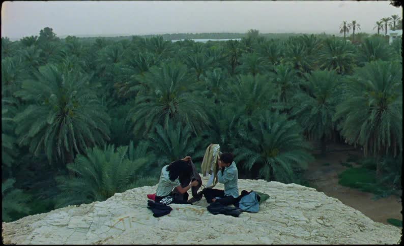 Two people sit on a rock by the forest sorting clothing