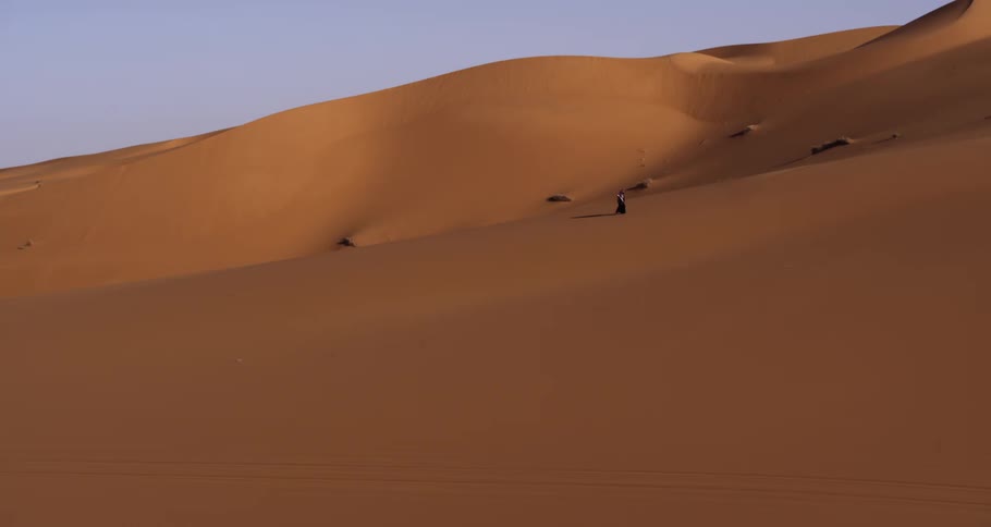 A person walking in a sand desert with some dunes behind