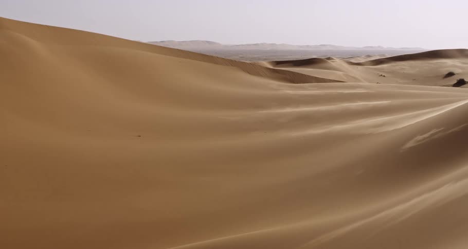 Aerial drone footage of the Empty Quarter in the Middle East, showcasing an endless desert expanse. The drone glides seamlessly through towering sand dunes, revealing the vast scale and breathtaking beauty of this untouched landscape