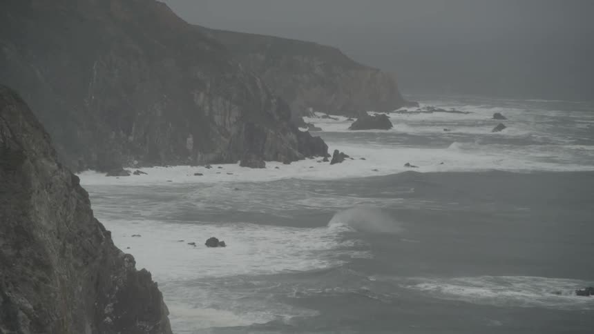 Waves crash against the rocks of the shore on a foggy day