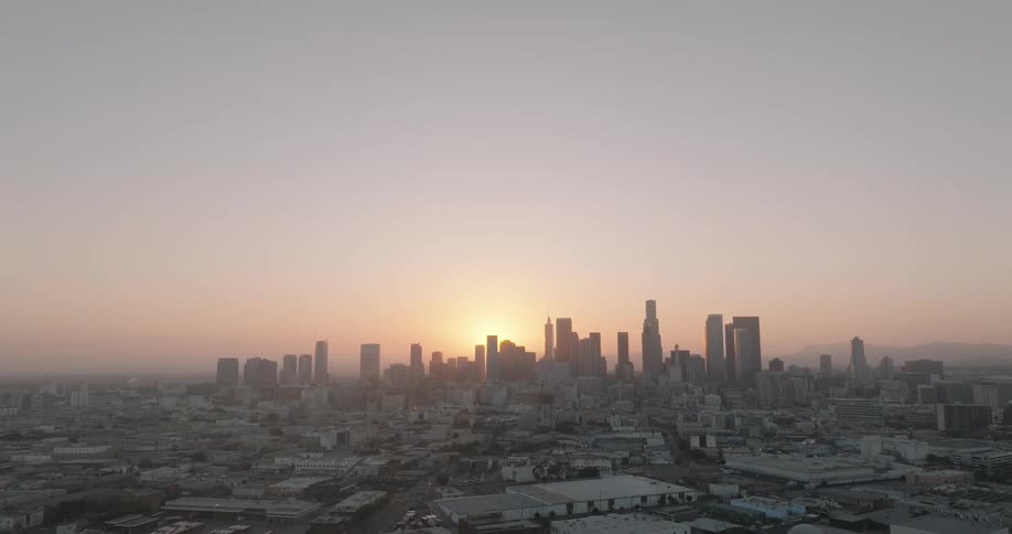 A panoramic view of a city skyline at sunset with the sun setting behind tall skyscrapers