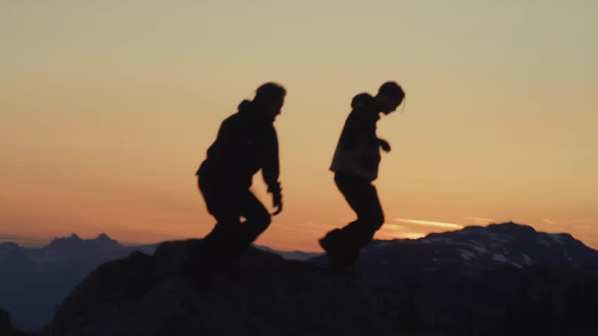 Silhouette of three people walking on a mountain with a reddish sky