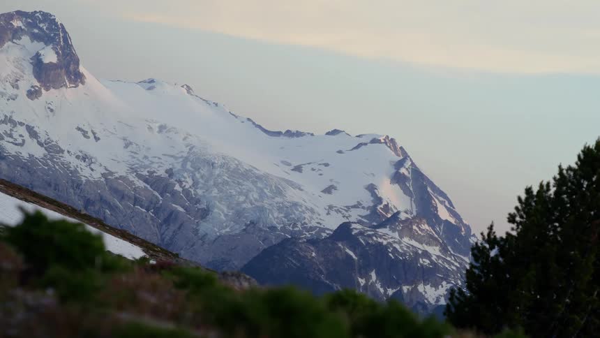 A majestic snowcapped mountain peak with a hint of pink in the sky suggesting a beautiful sunrise or sunset