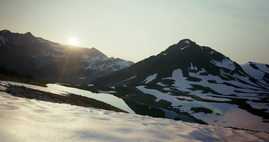 The sun peaks through a snow capped mountain