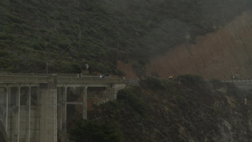 Motorcyclists cross a bridge while it rains